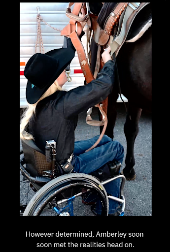 Amberley is sitting in a wheelchair and wearing a black blouse, blue jeans and a cowboy hat. She is putting a brown saddle on a horse.